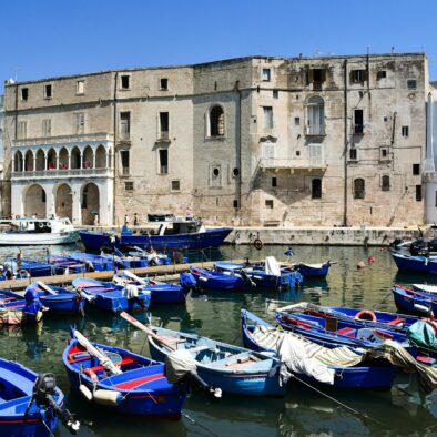Barche blu ormeggiate nel porticciolo di San Vito a Polignano con il monastero storico sullo sfondo e cielo limpido
