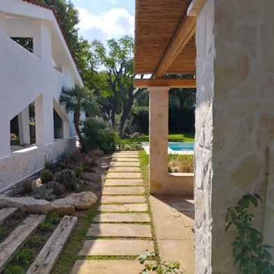 Camminamento in pietra tra il giardino e la piscina di Villa Agapanthus, circondato da piante mediterranee e pergolati in legno.