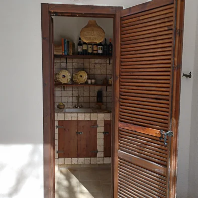 Porta in legno aperta sulla cucina in pietra della Villa Agapanthus con mensole rustiche e oggetti tipici pugliesi