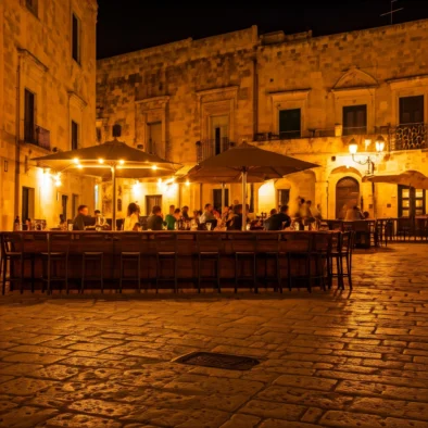 Tavolini all’aperto in una piazza pugliese illuminata di sera con luci calde e edifici storici in pietra