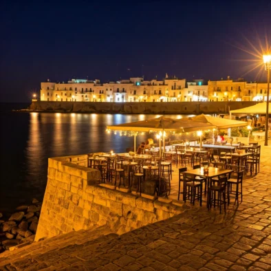 Tavoli illuminati per la cena sul lungomare di monopoli e con luci calde riflesse sul mare e centro storico sullo sfondo
