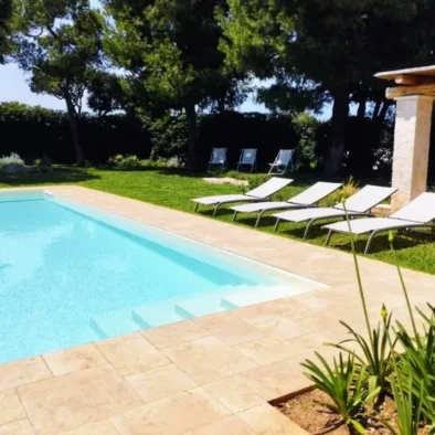 Piscina privata con lettini prendisole in una villa di lusso immersa nel verde a Monopoli, ideale per una vacanza di relax in Puglia.