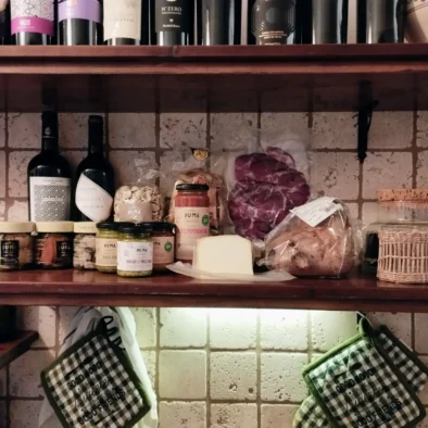 Mensole rustiche con bottiglie di vino, salumi, formaggi, conserve e taralli in una cucina tradizionale pugliese
