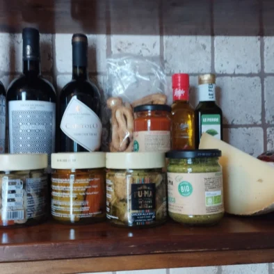 Mensola in cucina con bottiglie di vino pugliese, olio, conserve artigianali, formaggio e taralli tipici della regione