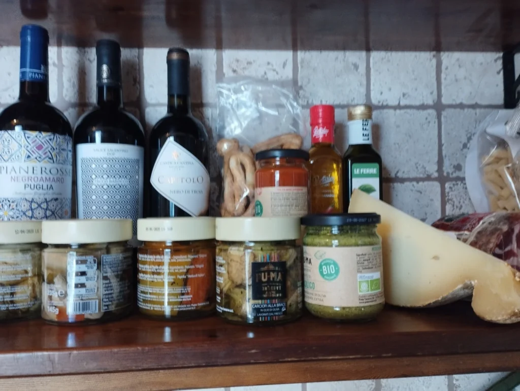 Mensola in cucina con bottiglie di vino pugliese, olio, conserve artigianali, formaggio e taralli tipici della regione
