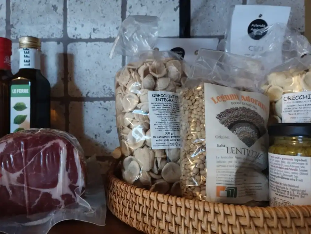 Selezione di prodotti tipici pugliesi con pasta artigianale, vino, salumi e ingredienti locali su mensola rustica