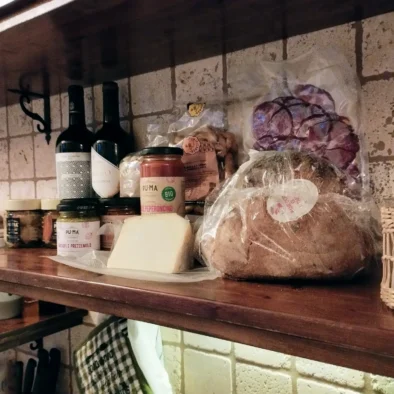 Pane, formaggio, vino, salumi e conserve disposti su mensola rustica nella cucina di Villa Agapanthus