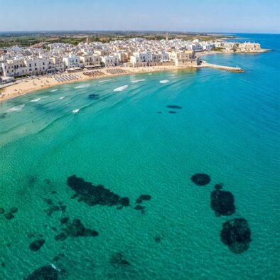 Vista aerea di un borgo pugliese con spiaggia dorata e mare turchese limpido, simbolo della bellezza mediterranea