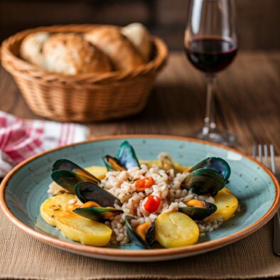 Piatto di riso, patate e cozze servito con pane pugliese e bicchiere di vino rosso su tavolo rustico