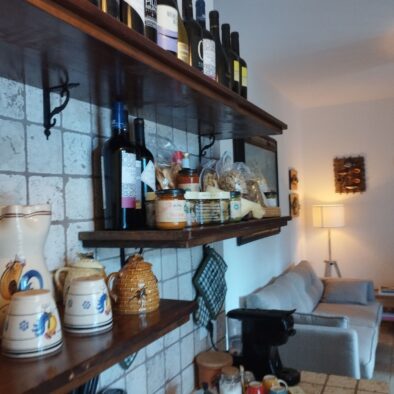 Scaffali con bottiglie di vino, ceramiche tipiche e luce calda nella cucina in pietra della Villa Agapanthus