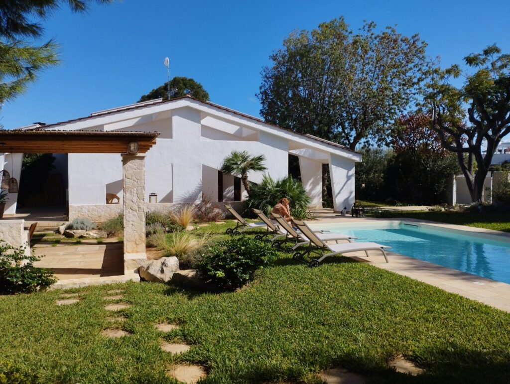 Vista panoramica della Villa Agapanthus con piscina privata, giardino curato, pergolato in legno e lettini prendisole