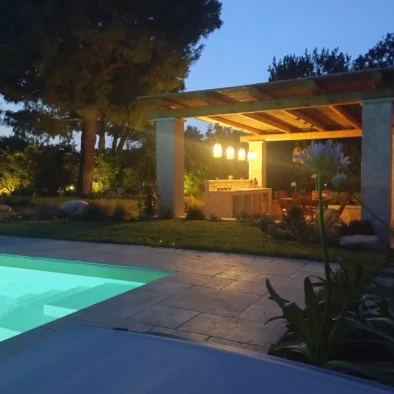 Vista serale della piscina illuminata e del patio con luci calde nella Villa Agapanthus, immersi nel giardino pugliese