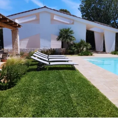 Piscina privata con lettini prendisole e vista sulla facciata bianca della Villa Agapanthus circondata da verde e silenzio