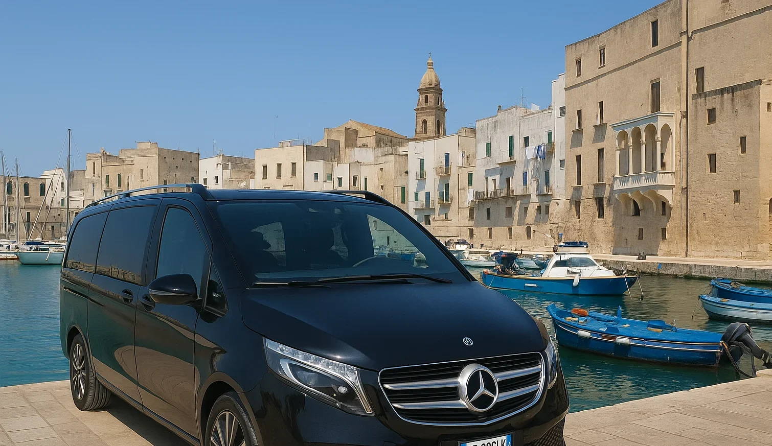 Luxury Mercedes V-Class minivan parked at Monopoli harbour pier, with boats and historic town behind